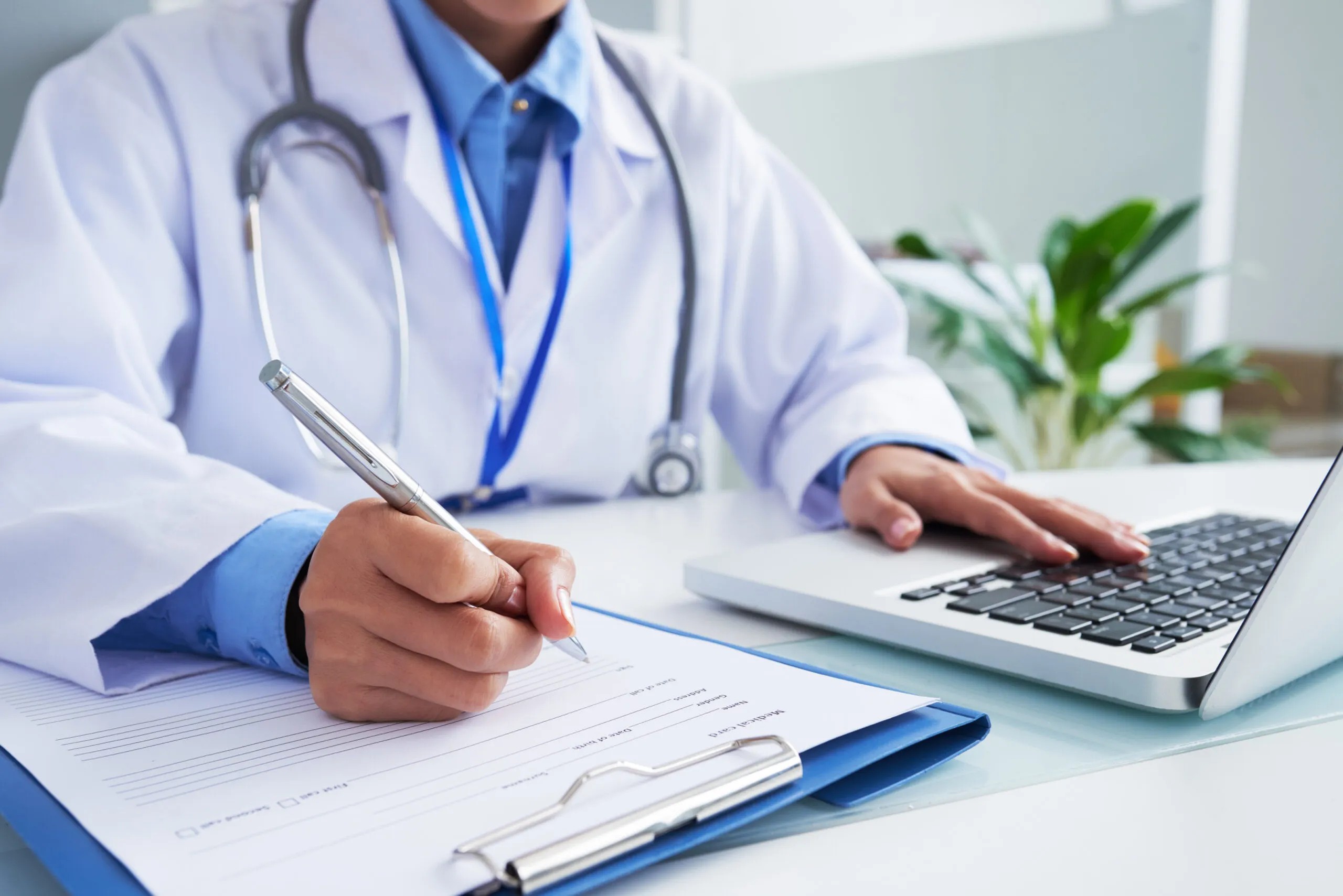 Médico registrando datos de un paciente en una ficha clínica junto a su laptop